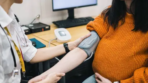 A doctor taking a pregnant woman's blood pressure using a machine