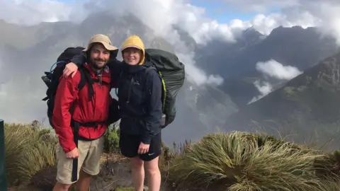 Megan Gardner A young couple poses while hiking up a picture-esque mountain, covered in cloud