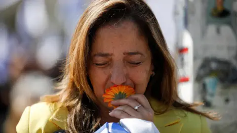 Reuters A woman kisses an orange flower in Tel Aviv, Israel, as Israelis gather to watch the funeral procession for the hostages Shiri, Ariel and Kfir Bibas (26 February 2025)