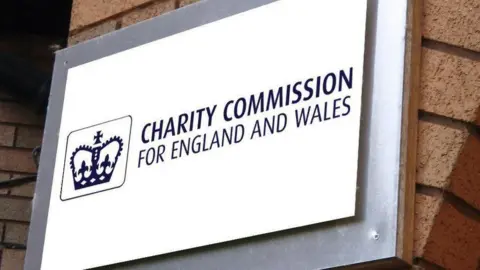 A white square sign with a logo of a crown next to the word charity commission for England and Wales 